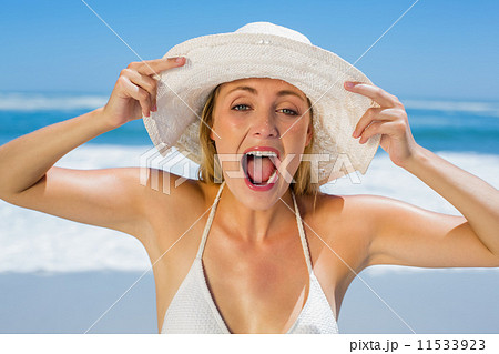 Smiling blonde in white bikini and sunhat on the beach 11533923