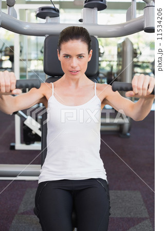 Fit brunette smiling at camera using weights machine for arms 11534206