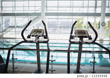 Cross trainer machines overlooking large swimming pool 11534448