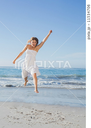 Beautiful blonde in white sundress jumping up on the beach 11534706