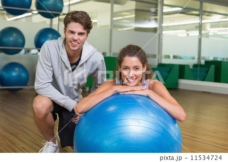 Fit woman leaning on exercise ball with trainer smiling at camer Fit woman leaning on exercise ball with trainer smiling at camer 11534724