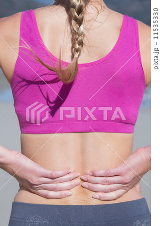 Fit woman touching her sore back on the beach Fit woman touching her sore back on the beach 11535330