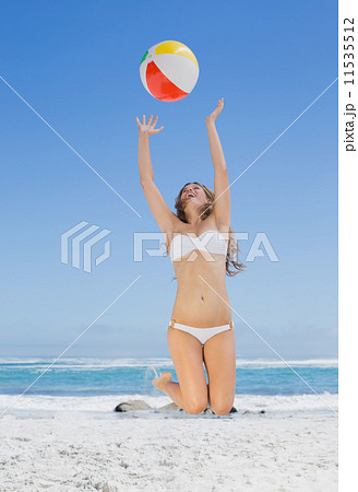 Fit blonde in white bikini throwing beach ball 11535512