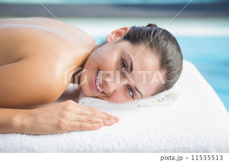 Smiling brunette lying on massage table poolside 11535513