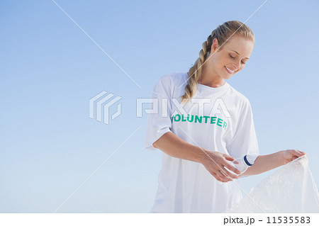 Blonde volunteer picking up trash on the beach 11535583