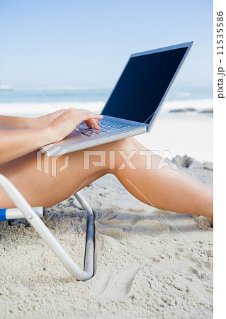 Woman sitting on beach using her laptop 11535586