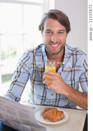 Casual smiling man having orange juice while reading newspaper 11535671