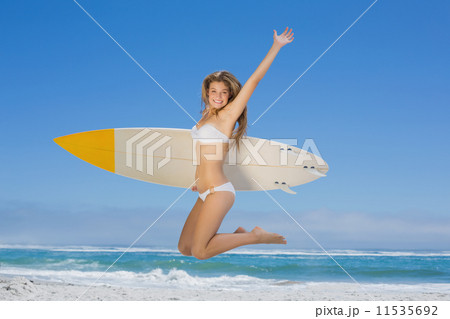 Smiling surfer girl holding her surfboard and jumping on the bea 11535692