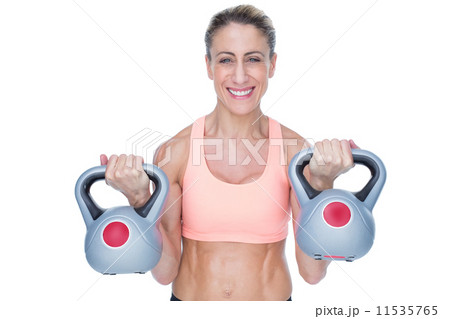 Smiling female crossfitter lifting kettlebells 11535765