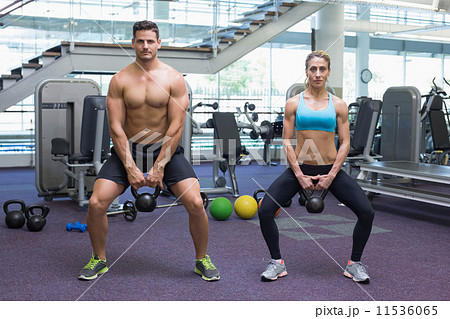 Bodybuilding man and woman lifting kettlebells in a squat Bodybuilding man and woman lifting kettlebells in a squat 11536065