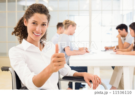 Casual businesswoman in wheelchair smiling at camera giving thum 11536110