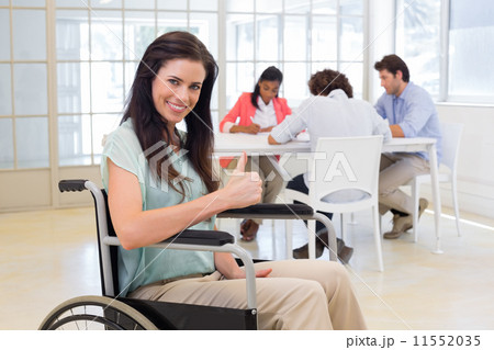 Attractive businesswoman in wheelchair gives thumbs up to camera Attractive businesswoman in wheelchair gives thumbs up to camera 11552035