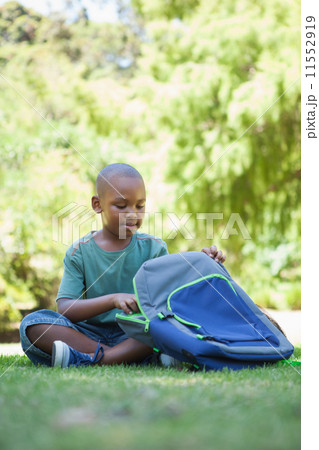 Happy schoolboy opening his schoolbag sitting on grass Happy schoolboy opening his schoolbag sitting on grass 11552919