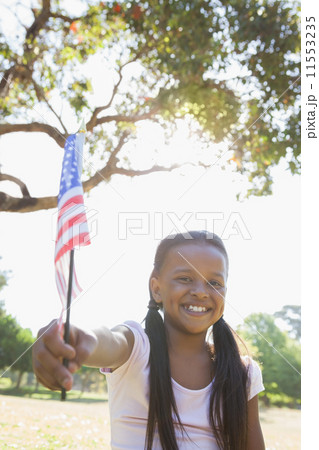 Little girl sitting on grass waving american flag 11553235