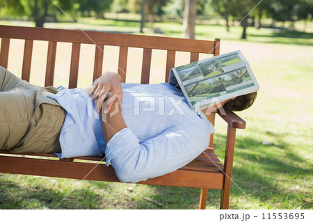 Man sleeping on park bench with newspaper over face 11553695