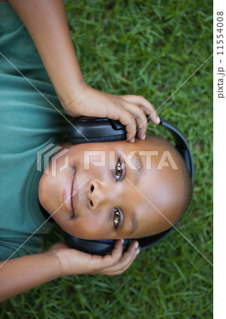 Little boy lying on grass listening to music smiling at camera 11554008