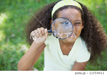 Young girl looking through magnifying glass in the park 11554011