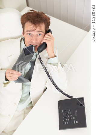 Young businessman speaks on phone, worries and bites tie Young businessman speaks on phone, worries and bites tie 11580733