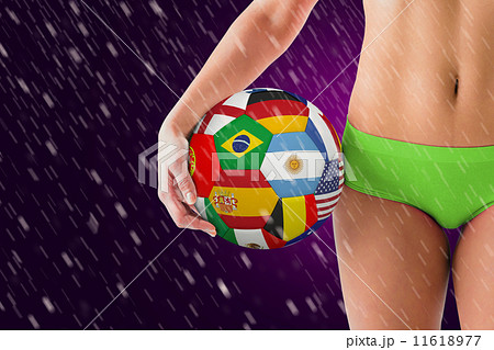 Composite image of fit girl in green bikini holding flag footbal 11618977