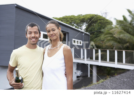 Multi-ethnic couple holding champagne in front of house 11627414