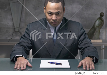 African businessman sitting at desk with paper and pen 11627550