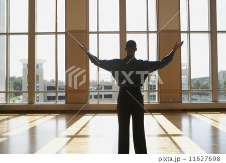 Businessman standing in sunlit room with arms outstretched  11627698