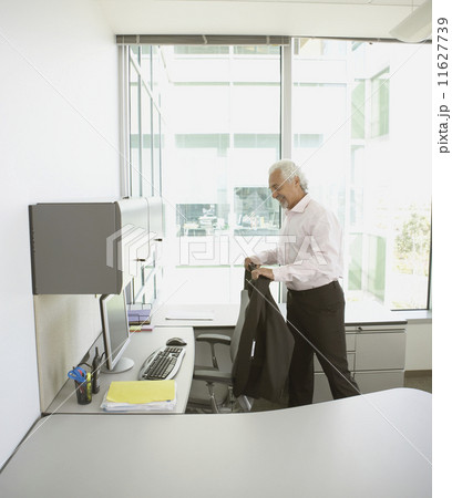 Middle-aged businessman hanging jacket on desk chair Middle-aged businessman hanging jacket on desk chair 11627739