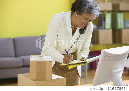 Mature woman on phone looking at computer screen and writing on legal pad 11627865