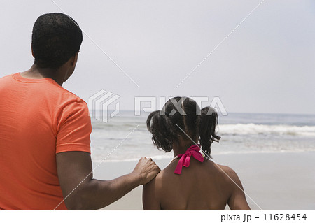 African father and daughter looking at ocean 11628454