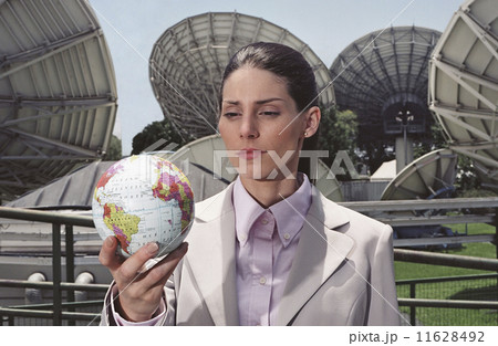 Hispanic businesswoman holding globe in front of satellite dishes 11628492