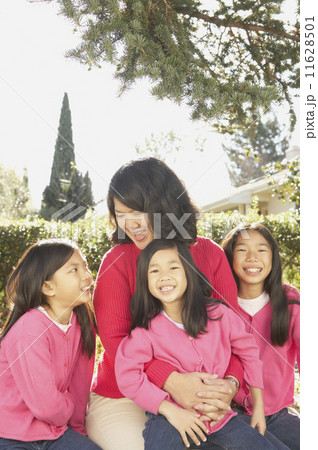 Asian mother with three young daughters laughing outdoors  11628501