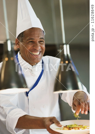 Mixed Race male chef garnishing plate of food 11628649