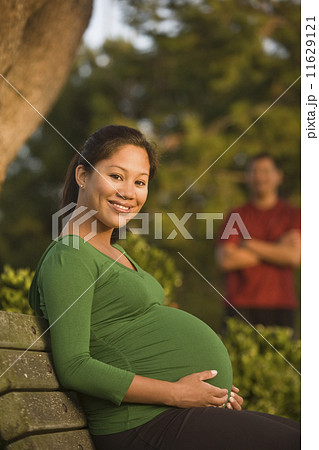 Pregnant Asian woman sitting on park bench 11629121