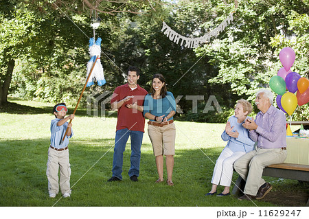 Family watching Hispanic boy hitting pinata at birthday party 11629247