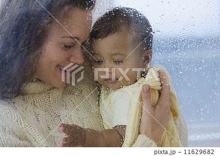 Hispanic mother holding baby behind rainy glass 11629682