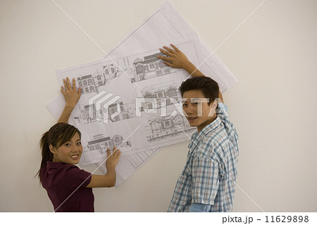 Asian couple holding blueprints on wall Asian couple holding blueprints on wall 11629898