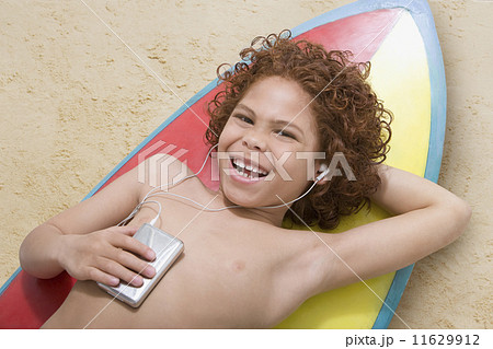 Mixed Race boy listening to mp3 player on surfboard Mixed Race boy listening to mp3 player on surfboard 11629912