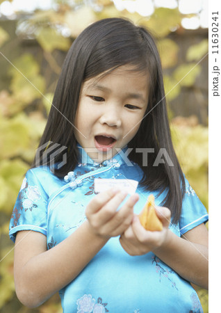 Young Asian girl holding a fortune cookie and reading her fortune  Young Asian girl holding a fortune cookie and reading her fortune  11630241