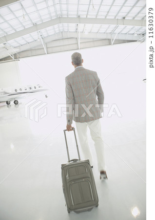 Man with suitcase walking out of airplane hanger  11630379