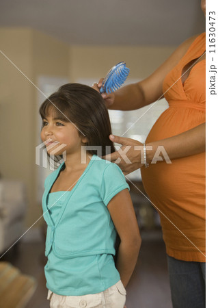 Pregnant Hispanic mother brushing daughter's hair 11630473