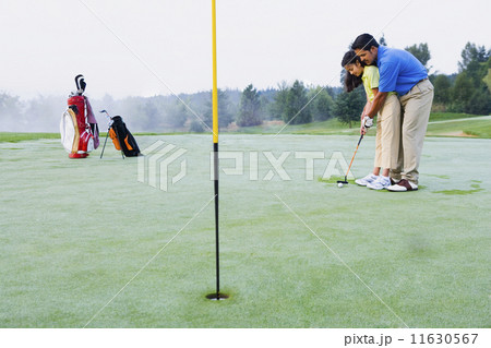 Hispanic father helping daughter play golf Hispanic father helping daughter play golf 11630567