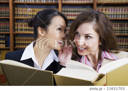 Multi-ethnic women whispering in law library  11631703