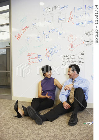 Two businesspeople sitting on floor in front of whiteboard wall Two businesspeople sitting on floor in front of whiteboard wall 11631764