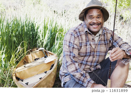 Middle aged African man with fishing gear next to canoe 11631899