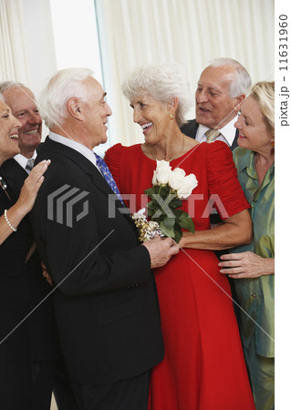 Senior man giving wife bouquet of flowers while friends watch 11631960