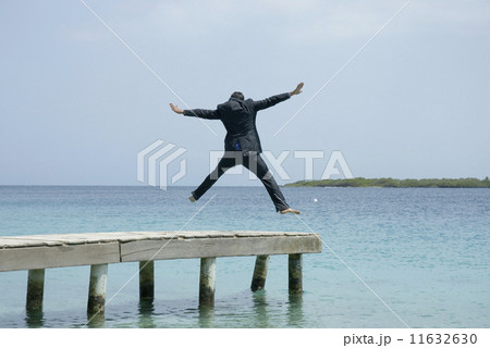 Hispanic businessman jumping on dock Hispanic businessman jumping on dock 11632630