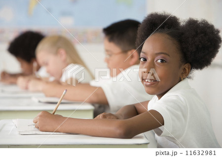Multi-ethnic children writing at desks in classroom 11632981