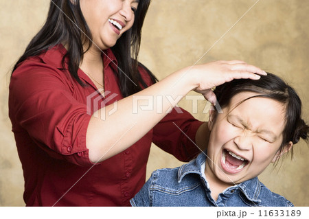 Asian mother fixing yelling daughter's hair Asian mother fixing yelling daughter's hair 11633189