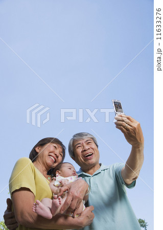 Asian grandparents holding baby grandchild and taking photograph Asian grandparents holding baby grandchild and taking photograph 11633276