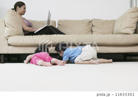 Mother working on laptop while children look under couch 11633301
